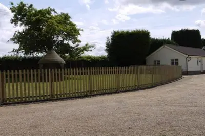 a fence in front of a yard with a tree at The Oaks, Luxury 2 bedroom cottage in a peaceful location in Haughley