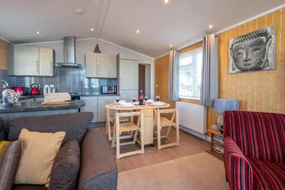 a living room with a couch and a kitchen at Chelsea Lodge - Aldeburgh Coastal Cottages in Sizewell