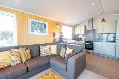 a living room with a couch and a kitchen at Chelsea Lodge - Aldeburgh Coastal Cottages in Sizewell