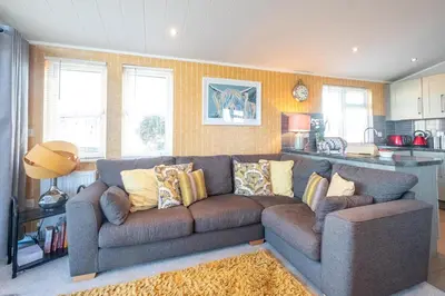 a living room with a couch and a kitchen at Chelsea Lodge - Aldeburgh Coastal Cottages in Sizewell