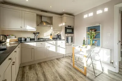 a kitchen with white cabinets and a white table at 1 Sanctuary Court - Aldeburgh Coastal Cottages in Thorpeness