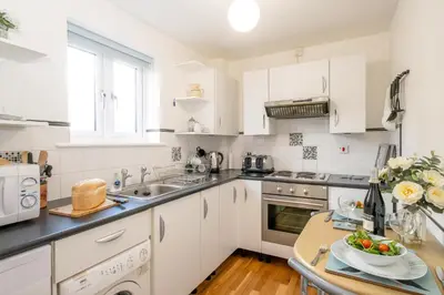 a kitchen with white cabinets and a table at The Britten - Aldeburgh Coastal Cottages in Aldeburgh