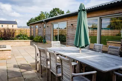 a wooden table with a green umbrella on a patio at Willow Cottage at Gravel Farm in Stretham