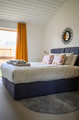 a bedroom with a large bed with an orange curtain at Willow Cottage at Gravel Farm in Stretham