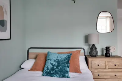 a bed with orange and blue pillows and a mirror at Studio Apartment - Central Chelmsford Location in Chelmsford