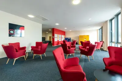 a waiting room with red chairs and tables at For Students Only Collegiate Athena Hall Ipswich in Ipswich
