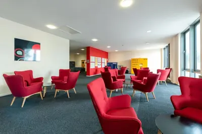 a waiting room with red chairs and tables at For Students Only Collegiate Athena Hall Ipswich in Ipswich