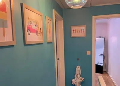 a hallway with a blue wall with pictures on it at Gulliver's Cottage in Frinton-On-Sea in Frinton-on-Sea