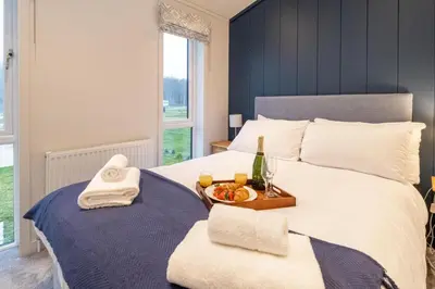 a bed with a tray of food and a bottle of champagne at Beach Lodge - Aldeburgh Coastal Cottages in Sizewell