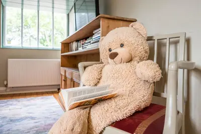 a teddy bear sitting on a bed holding a book at The Farmhouse Boundary Farm Framlingham in Woodbridge