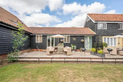 a patio with chairs and an umbrella in front of a house at The Cartlodge Boundary Farm, Framlingham in Woodbridge