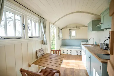 a small kitchen with a wooden table in a caravan at Sage Shepherds Hut Boundary Farm, Framlingham in Woodbridge