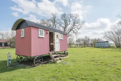 a small red house with a black roof in a field at Thyme Shepherds Hut Boundary Farm, Framlingham in Woodbridge
