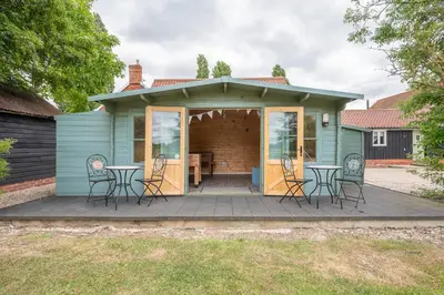 a blue house with chairs and tables on a deck at Thyme Shepherds Hut Boundary Farm, Framlingham in Woodbridge