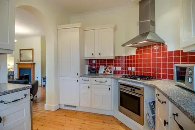 a kitchen with white cabinets and red tile on the wall at 2 Bed in Blythburgh oc-wag2 in Blythburgh