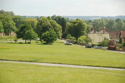 a large grassy field with cars parked on a road at Spadgers, a flax workers cottage next to fields in a Medieval Village in Long Melford