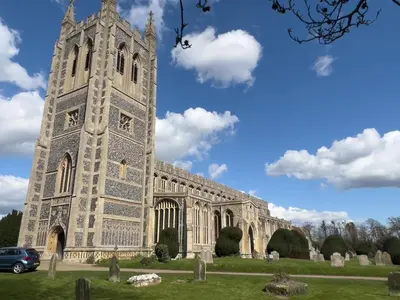 a large building with a clock tower in a cemetery at Spadgers, a flax workers cottage next to fields in a Medieval Village in Long Melford