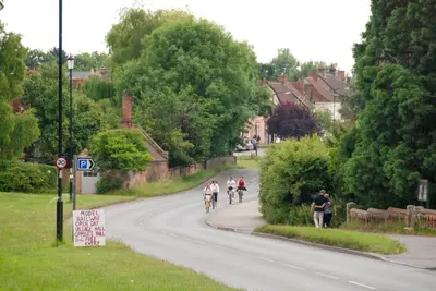 a group of people riding bikes down a road at Spadgers, a flax workers cottage next to fields in a Medieval Village in Long Melford