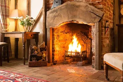 a brick fireplace with a fire in it at Spadgers, a flax workers cottage next to fields in a Medieval Village in Long Melford