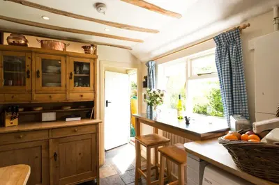 a kitchen with wooden cabinets and a counter with a window at Spadgers, a flax workers cottage next to fields in a Medieval Village in Long Melford