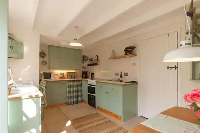 a large kitchen with green cabinets and a table at Romney, a cosy Victorian cottage in a picturesque Suffolk village in Cavendish