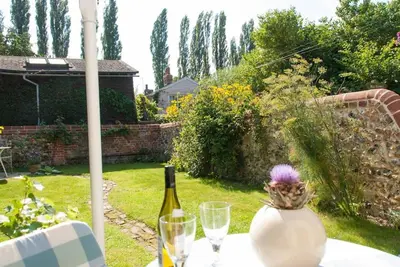 a table with a bottle of wine and a vase at Romney, a cosy Victorian cottage in a picturesque Suffolk village in Cavendish