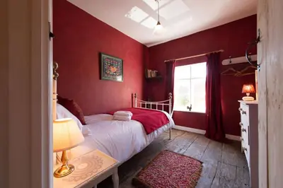 a bedroom with red walls and a bed and a window at Romney, a cosy Victorian cottage in a picturesque Suffolk village in Cavendish