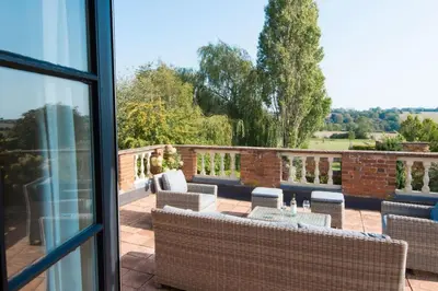 a patio with wicker chairs and tables on a balcony at The Old Steam Mill, luxury, spacious, beautiful grounds, stunning location in Hartest