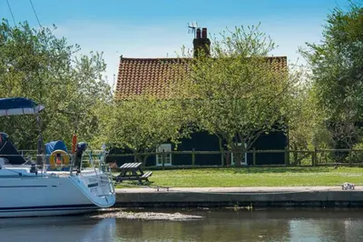 a boat docked next to a park with a building at Navigation Cottage on the Historic Sea Lock overlooking the Nature Reserve in Maldon