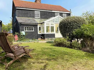 a wooden chair sitting in the yard of a house at Navigation Cottage on the Historic Sea Lock overlooking the Nature Reserve in Maldon