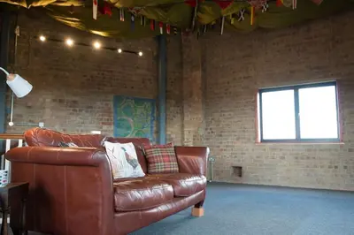 a brown leather couch in a room with a brick wall at The Hexagon, wow what a location, views over the Essex marshes and sea in West Mersea