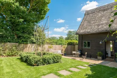 a cottage with a garden and a fence at Deepwell Granary is a lovely thatched barn with attached meadow woodland in Buxhall
