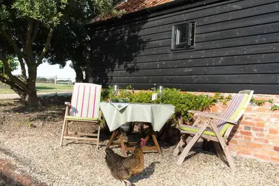 a table and two chairs and a chicken next to a building at Bromans Barn a beautiful cottage by the Sea and Cudmore Nature Reserve in West Mersea