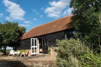 a black cottage with a white door and chairs at Bromans Barn a beautiful cottage by the Sea and Cudmore Nature Reserve in West Mersea
