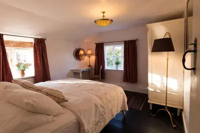 a bedroom with a large bed and two windows at Farm Cottage a cute C17th cottage a walk across the fields to a great pub in Edwardstone