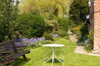 a table and a bench in a garden with flowers at Farm Cottage a cute C17th cottage a walk across the fields to a great pub in Edwardstone