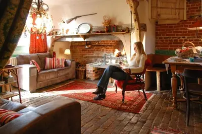 a woman sitting in a chair in a living room with a fireplace at Orchard Cottage cosy rustic comfort just across the fields to a great Pub in Edwardstone