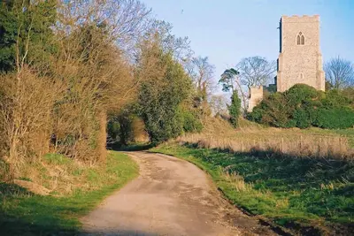 a dirt road with a tall tower in the distance at Rose Cottage rural cosiness with footpaths to the local Macro Brewery Pub in Edwardstone