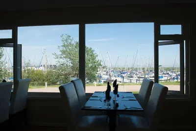 a dining room table with chairs and a view of a marina at The Wobbin, Remote, Comfort, Sea Views and the beautiful Essex Marshes in West Mersea