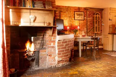 a brick fireplace in a kitchen with a table at The Bakery a honeymooners favourite cosy stylish with lovely walks and pubs in Edwardstone