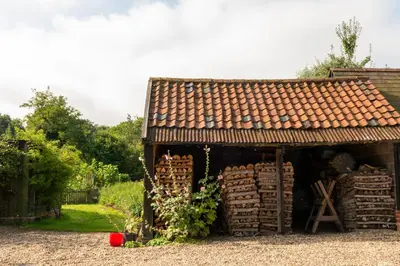 a building with a pile of wood in front of it at Mill Cottage set beside a Mill pond in a 70 acre Nature Reserve Bliss in Assington
