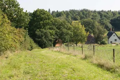 a field with a fence and a house in the background at Mill Cottage set beside a Mill pond in a 70 acre Nature Reserve Bliss in Assington
