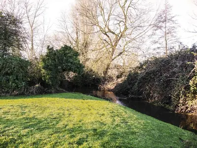 a grassy field next to a river with trees at Little Dene Lodge by The Suffolk Cottage Collection in Pakenham
