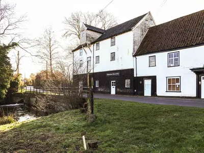 a white building with a black roof on a street at Little Dene Lodge by The Suffolk Cottage Collection in Pakenham