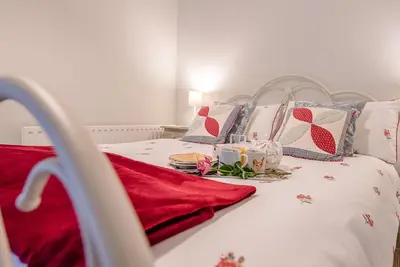 a white bed with red and blue pillows at 2 Riverside Cottages, Yoxford in Saxmundham