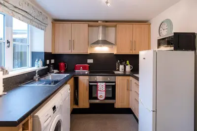 a kitchen with wooden cabinets and a white refrigerator at 2 Riverside Cottages, Yoxford in Saxmundham