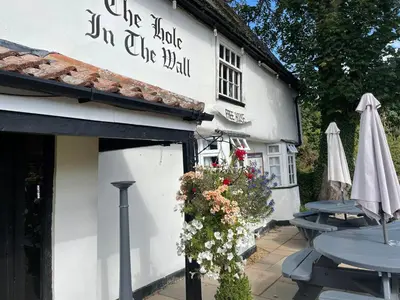 a white building with a table and chairs and an umbrella at The Hole In The Wall in Little Wilbraham