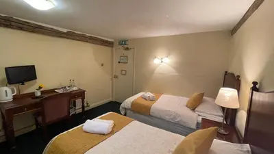 a room with two beds and a desk and a television at Crown Hotel in Downham Market