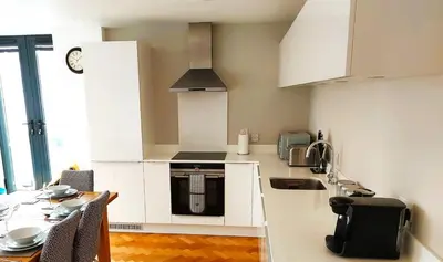 a kitchen with white cabinets and a table and a sink at Modern Town Centre Apartment in Chelmsford
