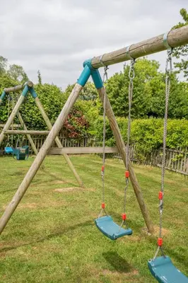 a swing set in a park with two swings at East Green Farm Cottage - Studio Barn - Aldeburgh Coastal Cottages in Kelsale